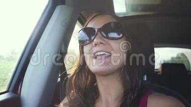 快乐的年轻女子戴着太阳镜<strong>坐在车上</strong>，乘客在阳光明媚的日子里欣赏着乡村的窗外，唱歌